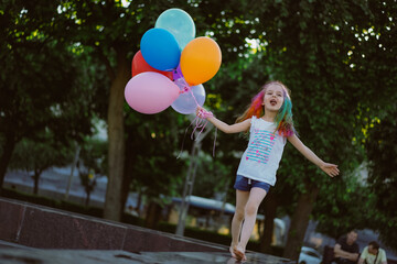 pretty little girl with colorful dyed hair holding bunch of baloons running along fountain parapet. Saint-Petersburg, Russia.Image with selective focus