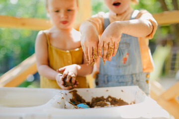 Happy children play with sand and water in sensory baskets on the outdoor sensory table, sensory early development, montessori. Baby hands with sand and water close up, soft focus