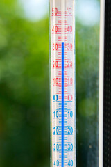 A Celsius thermometer on a window frame shows high temperatures of 35 degrees during an abnormal heat outside close-up.