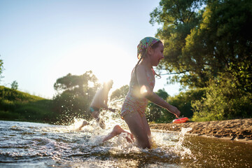 Happy children run from the shore into the water. Summer children's vacation on shore of a lake or river. boy and girl jump into water, swim and splash around at sunset. Active holidays. Dynamic image