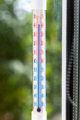 A Celsius thermometer on a window frame shows high temperatures during heat waves outside. Conceptual photo of heat, warm weather