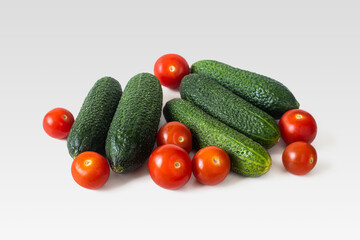 Green cucumbers and red cherry tomatoes on a light background