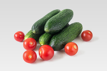 Ripe green cucumbers and red cherry tomatoes on a light background