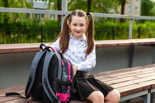 A Schoolgirl In A White Blouse And Black Skirt Sits On A Bench At The School Stadium, Pulls Out Of The Briefcase. Smiling. Daytime, Education