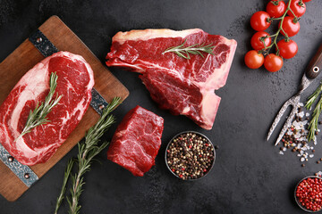 Assorted raw meat steaks. Japanese marble wagyu meat on a dark wooden board with spices, rosemary and fresh cherry tomatoes. Background image, copy space. Top view, flatlay