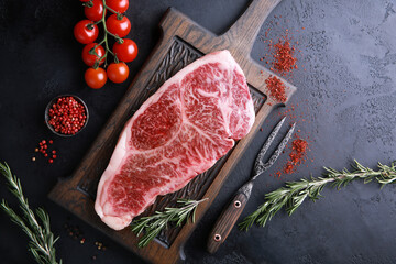 Raw meat steak. Japanese marble wagyu meat on a dark wooden board with spices, rosemary and fresh cherry tomatoes. Background image, copy space. Top view, flatlay