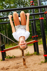 A girl in sports uniform hangs upside down on the turnstile. Sports ground, charging, warm-up, daytime, open air