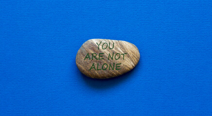You are not alone symbol. Beautiful stone with words You are not alone on beautiful blue background. Business, psychological and You are not alone concept.