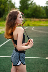 Young beautiful girl in sports top and shorts on the sports ground, posing on a sports ground. Daytime, fitness, open air, badminton, racket