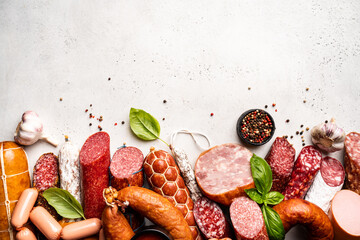 Set of different types of sausages, salami and smoked meat with basil and spices on white...