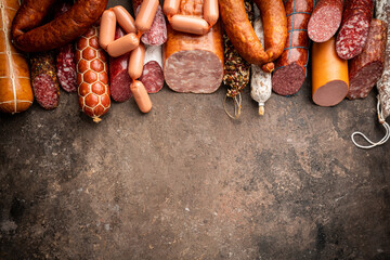 Set of different types of sausages, salami and smoked meat with basil and spices on brown stone...