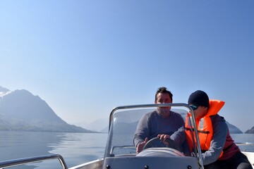 Father showing his son how to drive a motorboat on lake Lucerne. The son is wearing orange life...