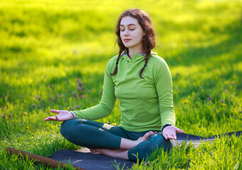 Girl in green park on grass does yoga meditation, active healthy lifestyle in pure nature outdoors