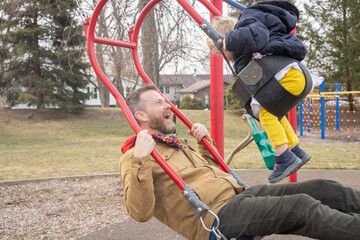 Daddy and toddler daughter on the swings at a park in the spring