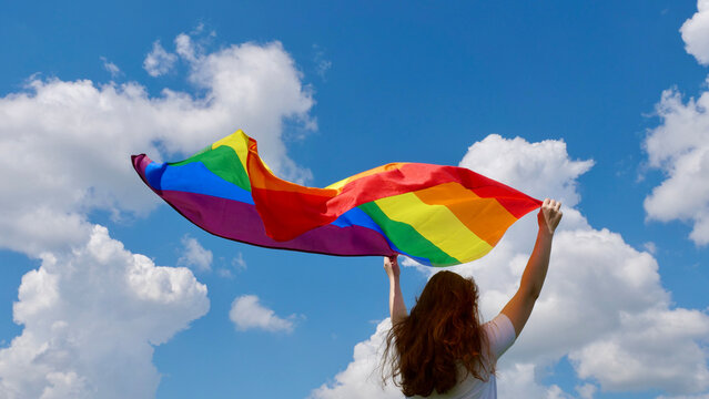 Bisexual woman lesbian holding a LGBT gender identity flag on a background of blue cloudy sky on a sunny windy summer day during the celebrating a gay parade Bisexuality Day or National Coming Out Day