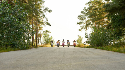 Young people driving in row on scooters in nature