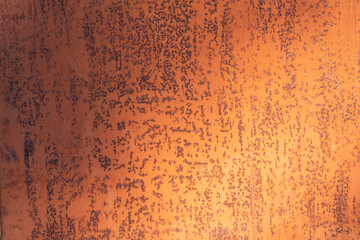 A steel sheet coated with brown paint is unevenly illuminated. There are multiple points of rust....