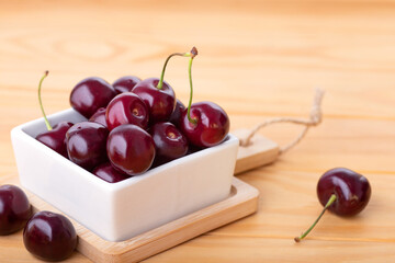 White square bowl with fresh red ripe cherry on wooden background.