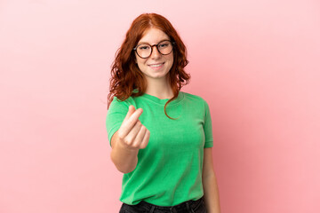 Teenager redhead girl over isolated pink background making money gesture