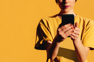 Modern woman browsing smartphone near yellow background