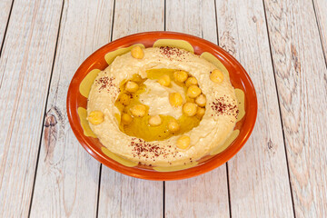 Chickpea hummus cooked with virgin olive oil, paprika grains in clay bowl on light wooden table
