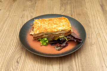 Rectangular portion of lasagna with several separate layers of meat and pasta sheets and the top with bechamel and gratin cheese
