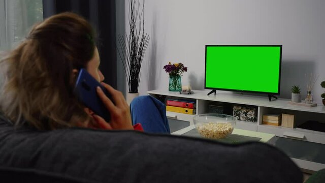 Woman Talking on Phone and watching Tv Green Screen. Phone Conversation Movie time Sports Match, News, Sitcom TV Show in the evening.