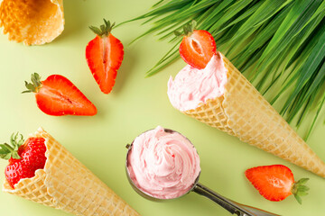 Strawberry ice cream in a waffle cone and spoon on a green background. Fresh strawberries. View from above. Summer natural dessert