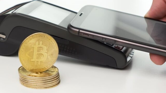 Close up man hand contactless paying by smartphone and bitcoin coins on the table