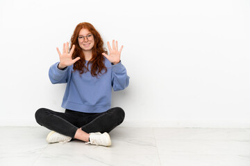 Fototapeta na wymiar Teenager redhead girl sitting on the floor isolated on white background counting ten with fingers