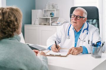 Senior physician writing on document during consultation with anonymous patient