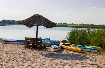 Sand beach by the lake. There is a straw umbrella, old pallets and boats on the beach