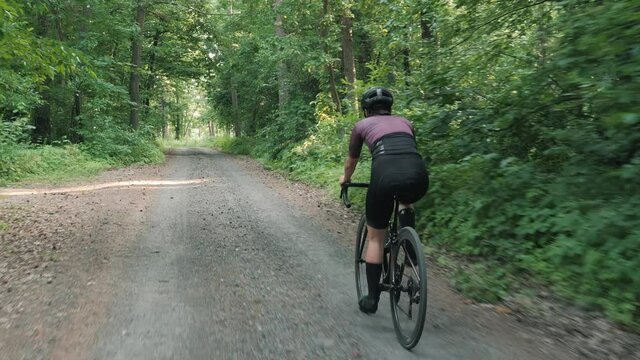 Woman riding road bike along gravel road. Cycling on forest road. Cyclist on forest track