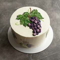 White birthday cake with painted blue grapes on grey background. Buttercream. Close up, copy space. top view.