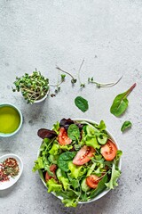 Fresh salad with fresh vegetables, ripe tomatoes, cucumber, lettuce and microgreen  in a bowl on a gray background. Healthy raw food concept. Place for text, copy space.