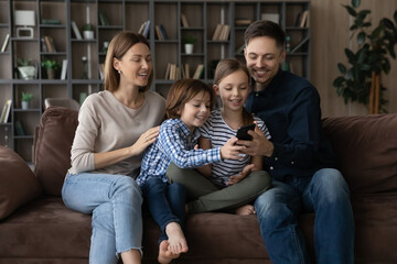 Happy young Caucasian family with two small children relax on sofa talk speak on video call on...