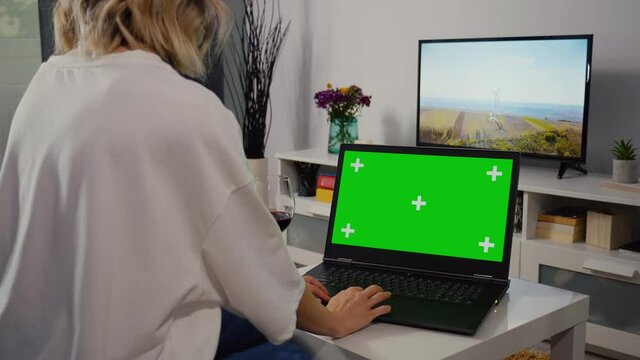 Woman make online shopping on laptop with Greenscreen and Chroma Key Mock Up with Tracking Markers and Alpha Matte. Female Using Laptop and Drink Wine in the Evening.
