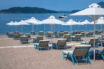 Empty white sun loungers without people under umbrellason the pebble beach by the sea.
