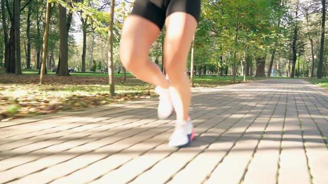 Close up of energy muscular woman in sport sneakers running outdoors. Focus of strong female legs. Young lady having morning workout at city park.