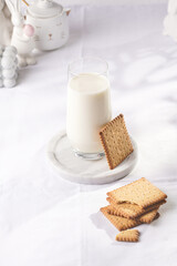 A glass of milk on a marble plate on a white table cloth and freshly baked cookies
