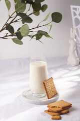 A glass of milk on a marble plate on a white table cloth and freshly baked cookies