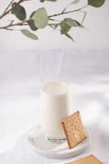 A glass of milk on a marble plate on a white table cloth and freshly baked cookies