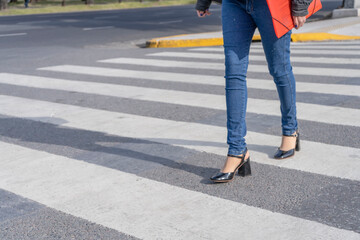 Woman's legs with shoes and pants crossing a street on the pedestrian path or zebra crossing.