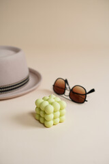 A pastel green bubble candle on an beige colored seamless background, and sunglasses and a hat
