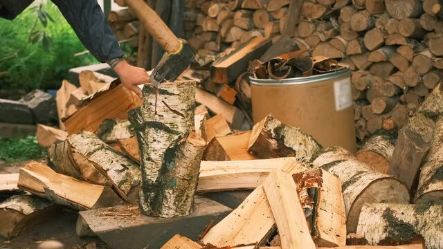 Close-up of a man chopping a log and chopping it in half with an ax. A young man works in the courtyard of a country house, chopping wood with a cleaver for kindling a fireplace. 