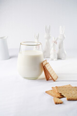 A glass of milk on the white table cloth and freshly baked cookies leaning on the glass