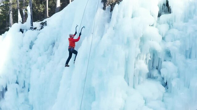 Aerial shot of an ice slope bumps, ridges, and icicles by which climbing up Caucasian man using traction ice tool technique
