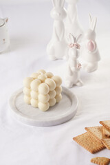 One white bubble candle on white table cloth, surrounded by easter bunny figurines