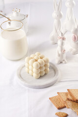 One white bubble candle on white table cloth, surrounded by milk and easter bunny figurines