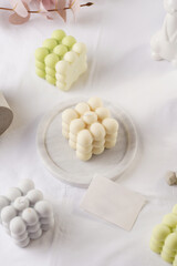 Several bubble candles, grey, patel green and beige on white table cloth